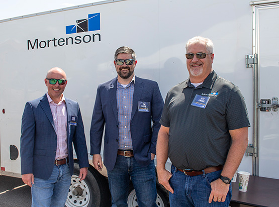 Three male team members in front of trailer that has the Mortenson logo on it